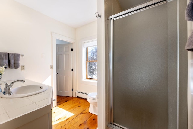 bathroom featuring a baseboard radiator, toilet, wood finished floors, a sink, and a stall shower