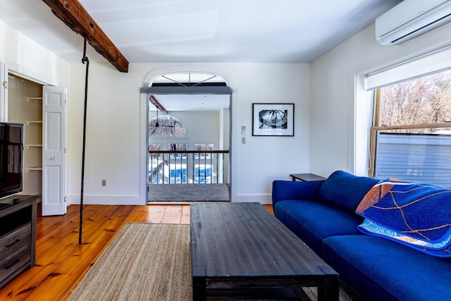 living room with beam ceiling, a wall mounted air conditioner, hardwood / wood-style flooring, and baseboards