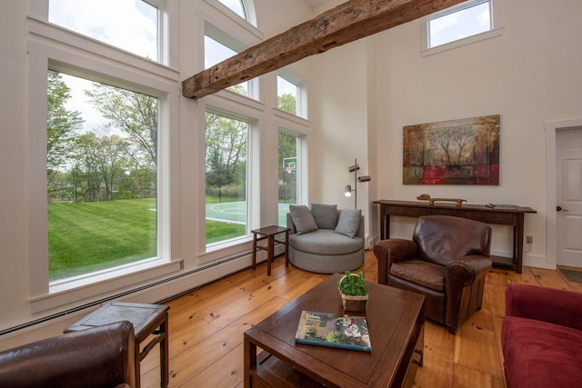 living room with a towering ceiling, light wood finished floors, and a baseboard radiator