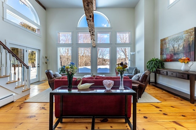 living area featuring wood-type flooring, baseboard heating, a high ceiling, baseboards, and stairs