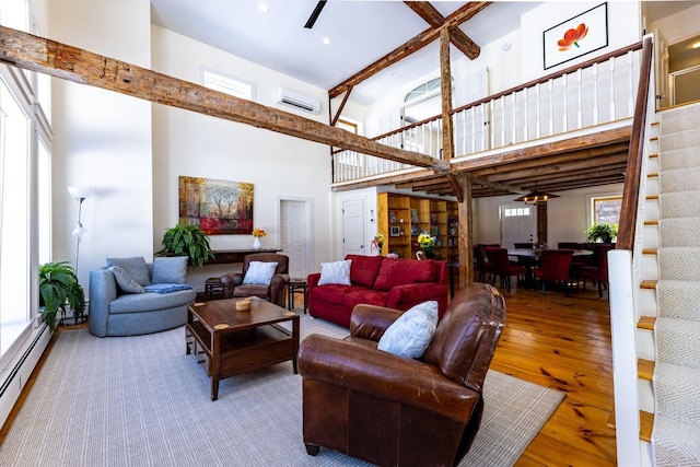 living room with beam ceiling, baseboard heating, ceiling fan, wood finished floors, and a wall mounted air conditioner