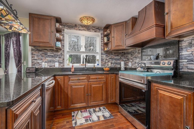 kitchen featuring dark wood finished floors, custom range hood, appliances with stainless steel finishes, open shelves, and a sink