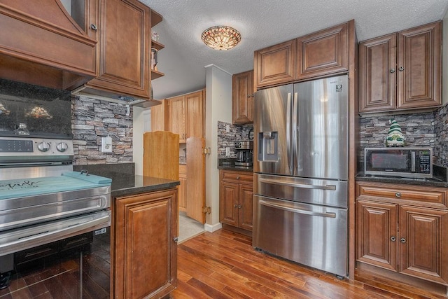 kitchen featuring a textured ceiling, stainless steel appliances, wood finished floors, backsplash, and brown cabinetry