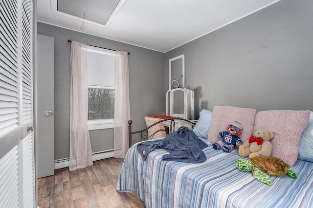 bedroom featuring a baseboard radiator, a baseboard heating unit, wood finished floors, ornamental molding, and attic access