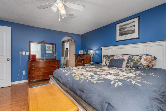 bedroom featuring arched walkways, a ceiling fan, a textured ceiling, wood finished floors, and baseboards