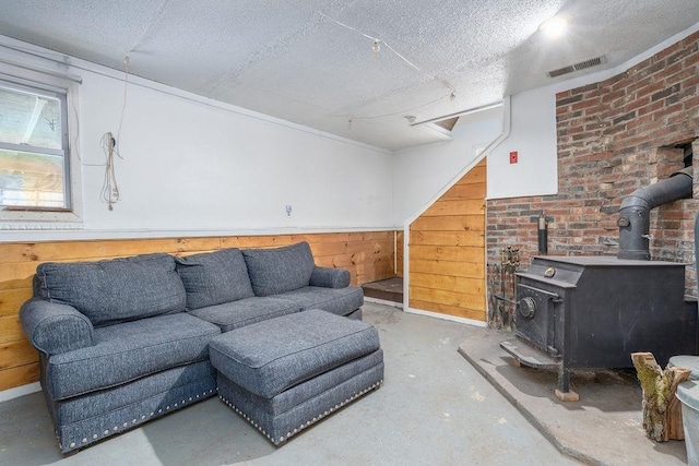 living room with a textured ceiling, a wood stove, unfinished concrete flooring, and visible vents