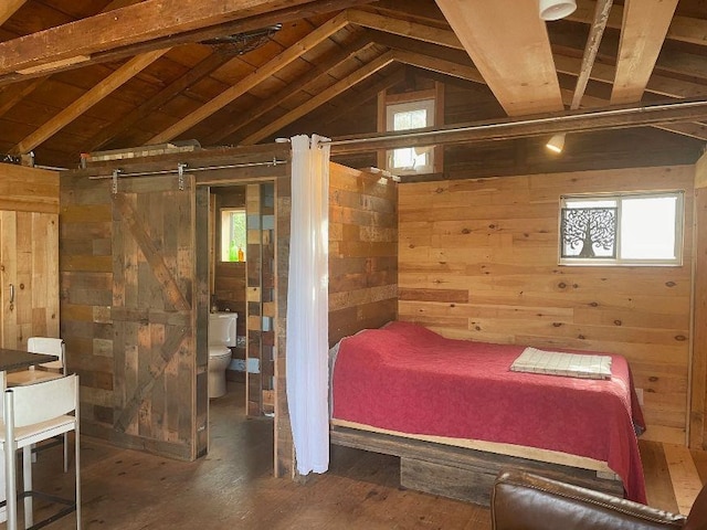 bedroom with lofted ceiling, a barn door, wood walls, and wood finished floors