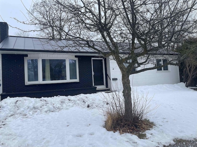 snow covered property featuring metal roof, brick siding, a chimney, and a standing seam roof