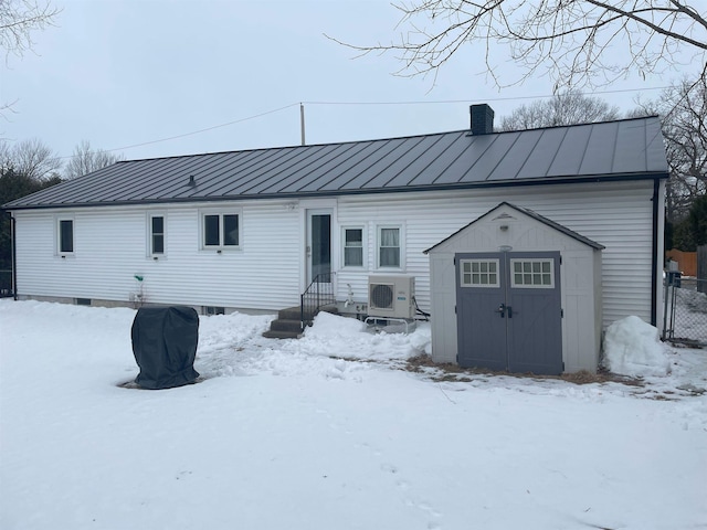 snow covered house featuring an outbuilding, a standing seam roof, entry steps, a storage unit, and metal roof