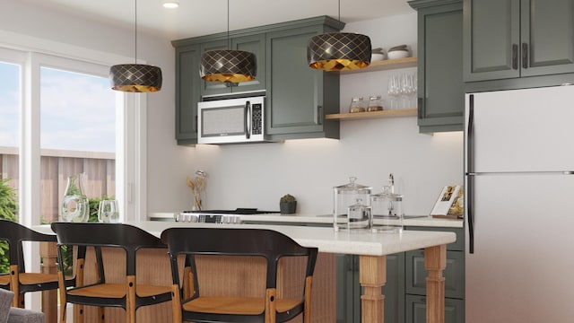 kitchen with light countertops, stainless steel microwave, hanging light fixtures, freestanding refrigerator, and green cabinetry