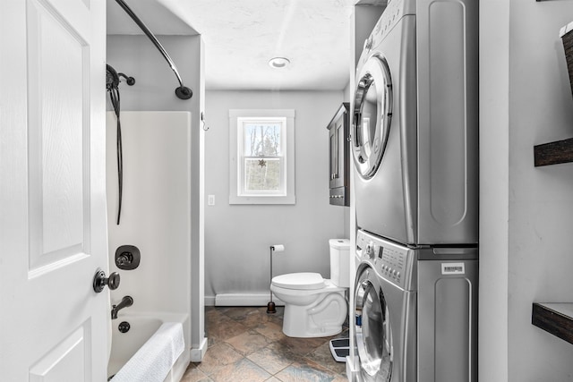 bathroom featuring stacked washer and clothes dryer, toilet, stone finish floor, shower / tub combination, and baseboards