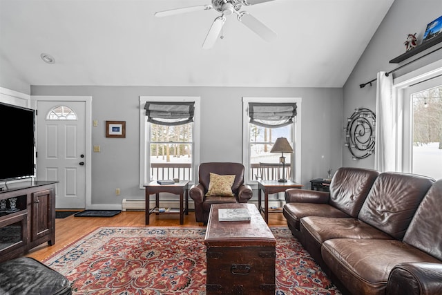 living area featuring a baseboard heating unit, a wealth of natural light, light wood-type flooring, and vaulted ceiling