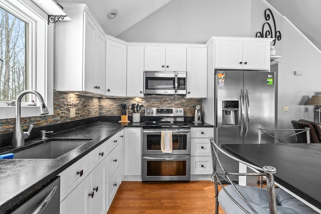 kitchen with lofted ceiling, wood finished floors, a sink, appliances with stainless steel finishes, and dark countertops