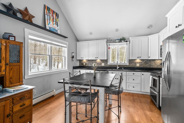 kitchen with lofted ceiling, a sink, appliances with stainless steel finishes, baseboard heating, and dark countertops