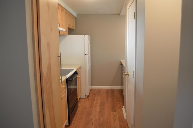 kitchen featuring baseboards, light wood finished floors, light brown cabinetry, light countertops, and black electric range oven