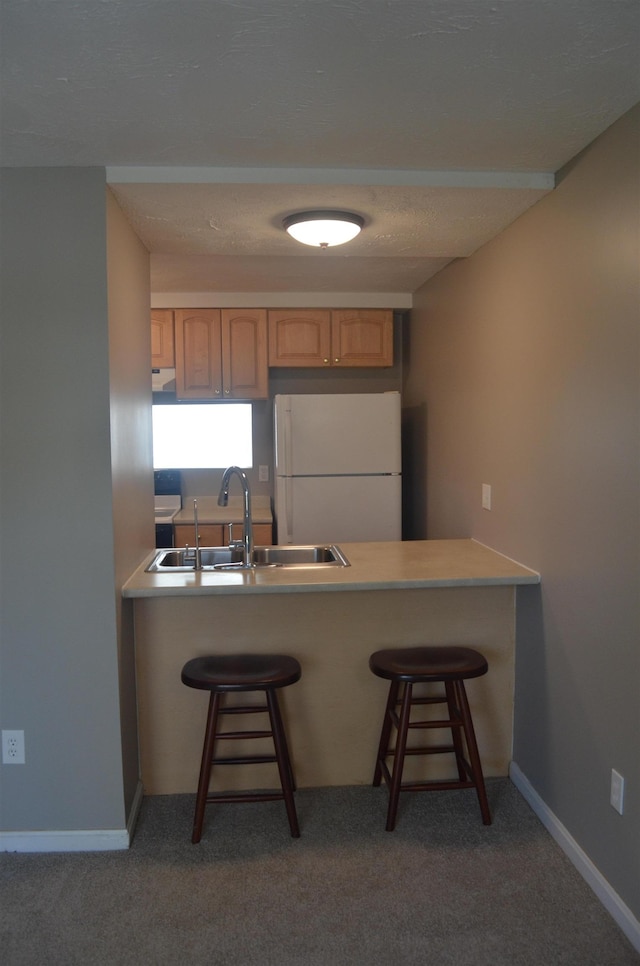 kitchen with light brown cabinets, a breakfast bar, carpet flooring, freestanding refrigerator, and a sink