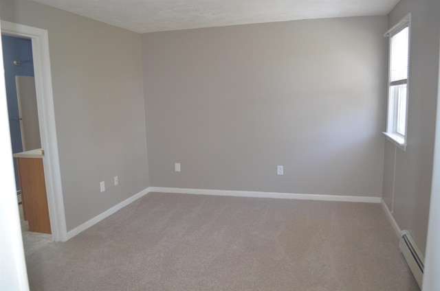 spare room featuring plenty of natural light, light colored carpet, baseboards, and a baseboard radiator