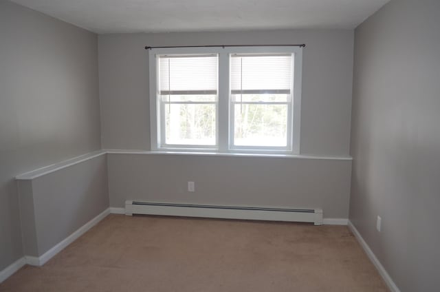 spare room with a baseboard heating unit, baseboards, and light carpet