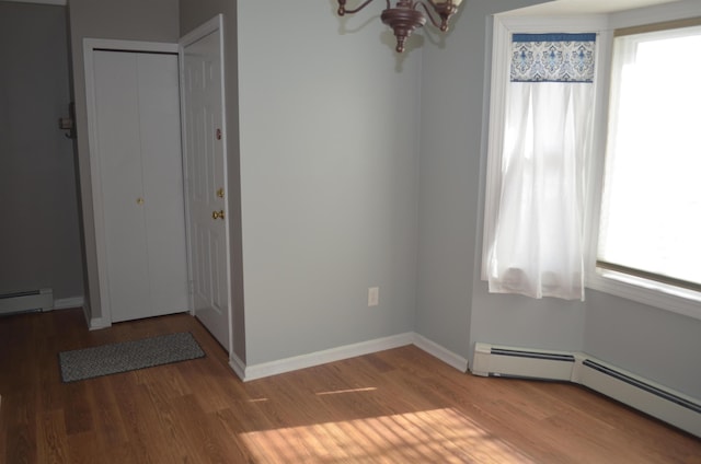 empty room featuring a baseboard heating unit, baseboards, an inviting chandelier, and wood finished floors