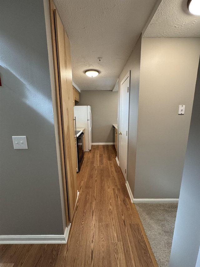 hallway with baseboards, a textured ceiling, and wood finished floors