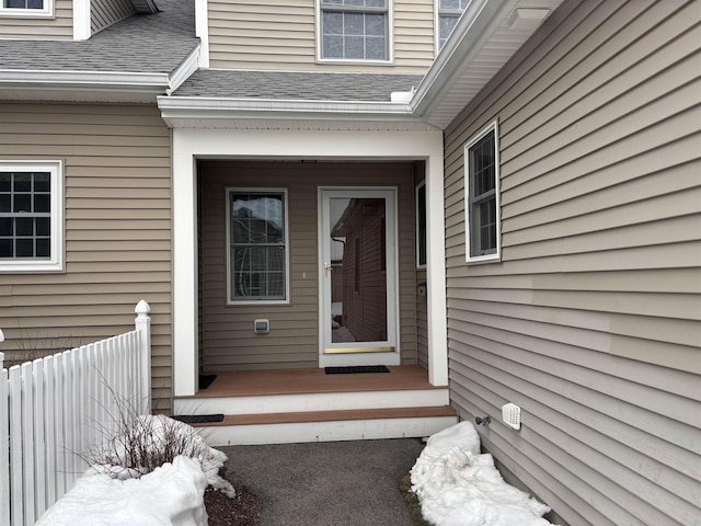 doorway to property featuring covered porch, a shingled roof, and fence