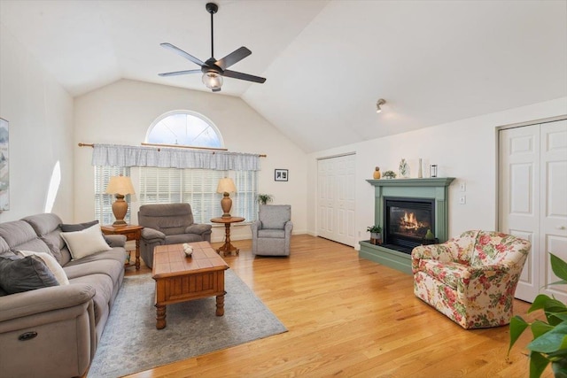 living area with ceiling fan, light wood-style floors, a glass covered fireplace, and high vaulted ceiling