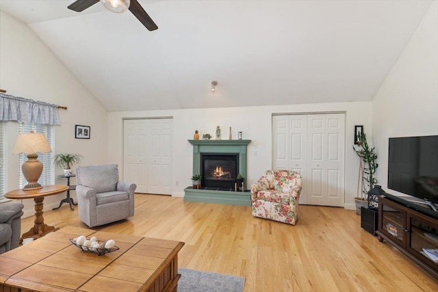 living area with a warm lit fireplace, light wood-type flooring, and lofted ceiling