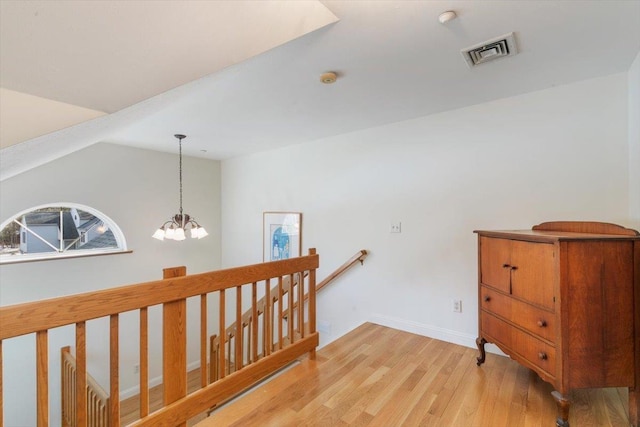 hallway featuring visible vents, an upstairs landing, a notable chandelier, light wood-style floors, and lofted ceiling