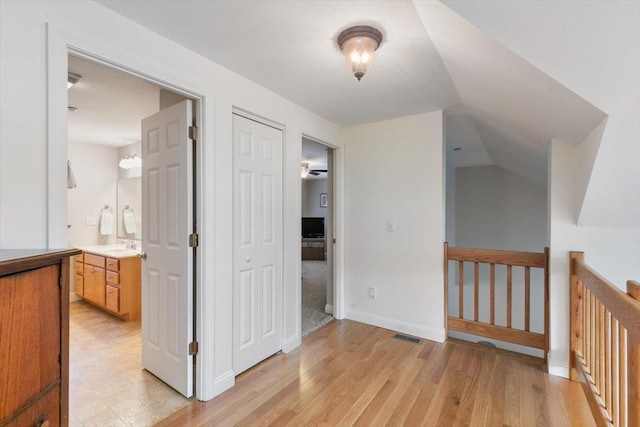 hall with visible vents, an upstairs landing, light wood-style floors, baseboards, and vaulted ceiling