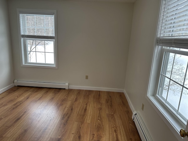 spare room with a baseboard heating unit, wood finished floors, and baseboards