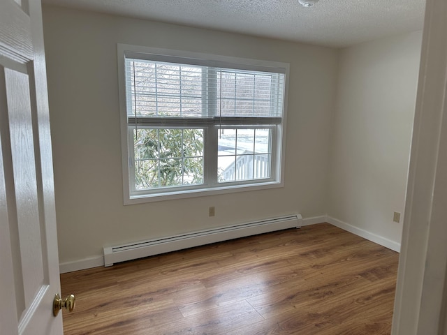 spare room with a textured ceiling, a baseboard heating unit, baseboards, and wood finished floors