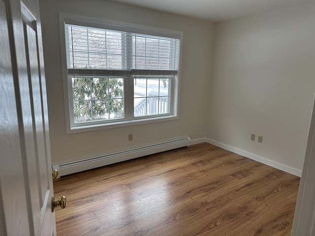 empty room with a baseboard radiator, baseboards, and wood finished floors