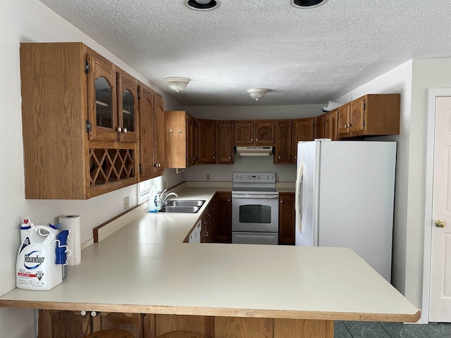 kitchen with white appliances, a peninsula, a sink, light countertops, and under cabinet range hood