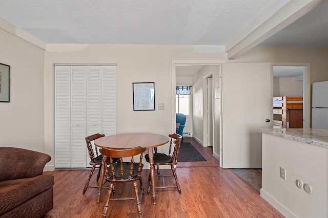 dining space with baseboards, a textured ceiling, and wood finished floors