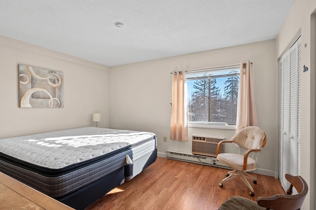 bedroom featuring a textured ceiling, an AC wall unit, baseboards, and wood finished floors