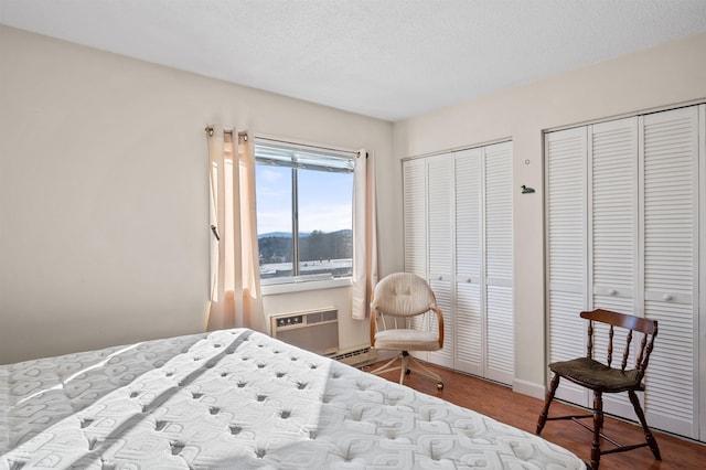 bedroom featuring a textured ceiling, two closets, a wall unit AC, and wood finished floors