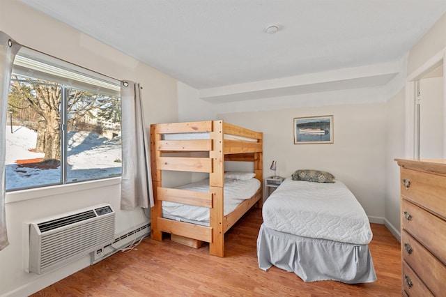 bedroom featuring baseboard heating, a wall mounted AC, light wood-type flooring, and baseboards