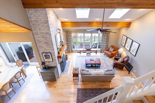 living area with beam ceiling, light wood finished floors, a skylight, and a ceiling fan