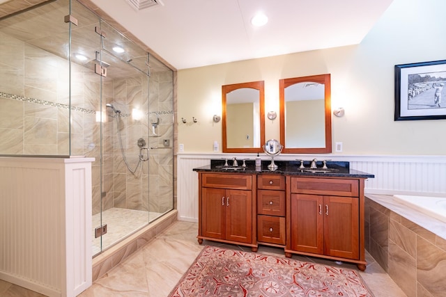 full bath with double vanity, a stall shower, a wainscoted wall, and a sink