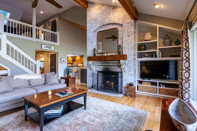 living room with stairway, wood finished floors, lofted ceiling with beams, a fireplace, and ceiling fan