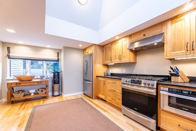 kitchen featuring stainless steel appliances, light wood finished floors, dark countertops, and wall chimney range hood