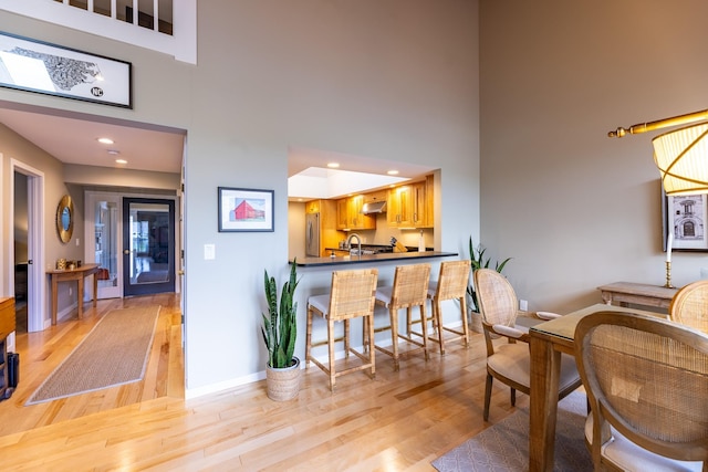 dining room with light wood finished floors, recessed lighting, baseboards, and a towering ceiling