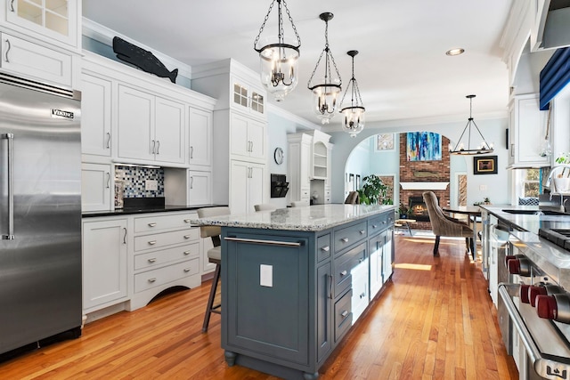 kitchen featuring a fireplace, ornamental molding, white cabinetry, light wood-type flooring, and stainless steel built in refrigerator