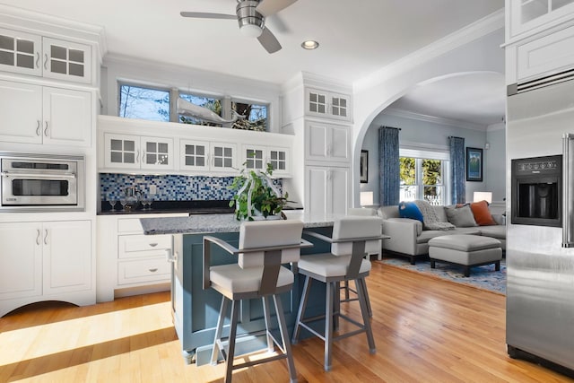 kitchen featuring tasteful backsplash, stainless steel built in fridge, ornamental molding, a kitchen breakfast bar, and arched walkways