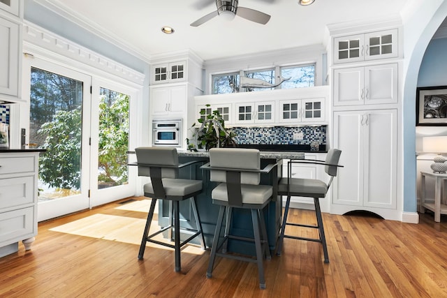 interior space featuring backsplash, dark countertops, white cabinetry, arched walkways, and crown molding