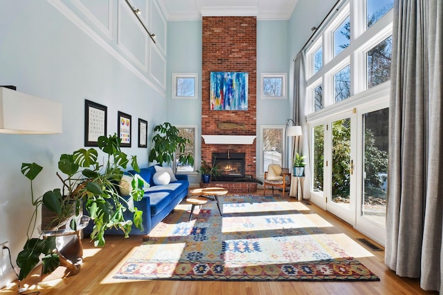 living room with wood finished floors, visible vents, a high ceiling, a fireplace, and ornamental molding