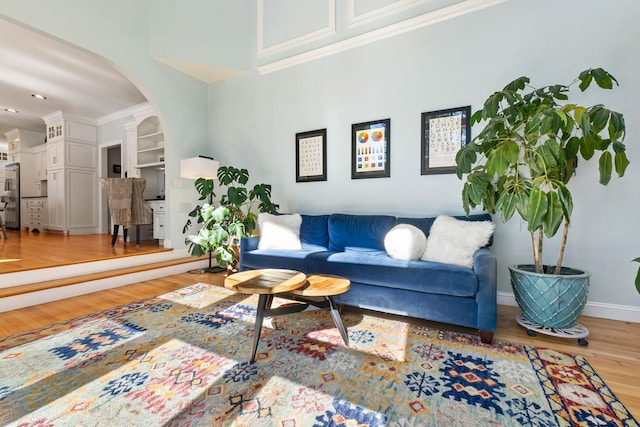 living room with built in features, baseboards, light wood finished floors, arched walkways, and crown molding