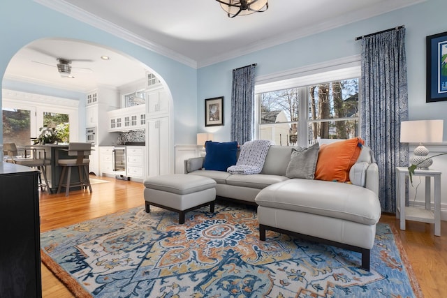 living room with wine cooler, a healthy amount of sunlight, crown molding, and light wood-style floors