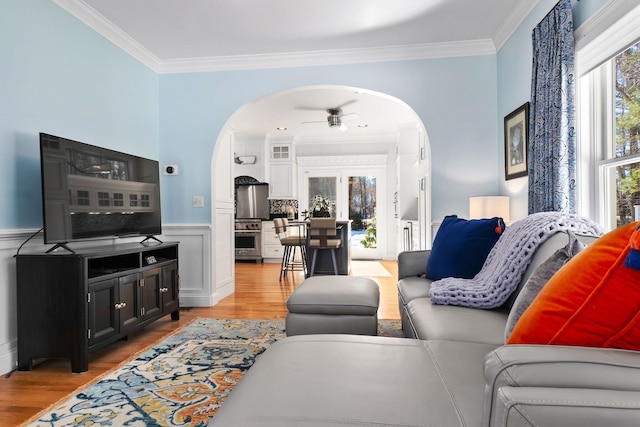 living room featuring light wood-style flooring, arched walkways, a wainscoted wall, and ornamental molding