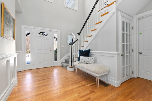 foyer with a decorative wall, a high ceiling, stairs, and light wood finished floors